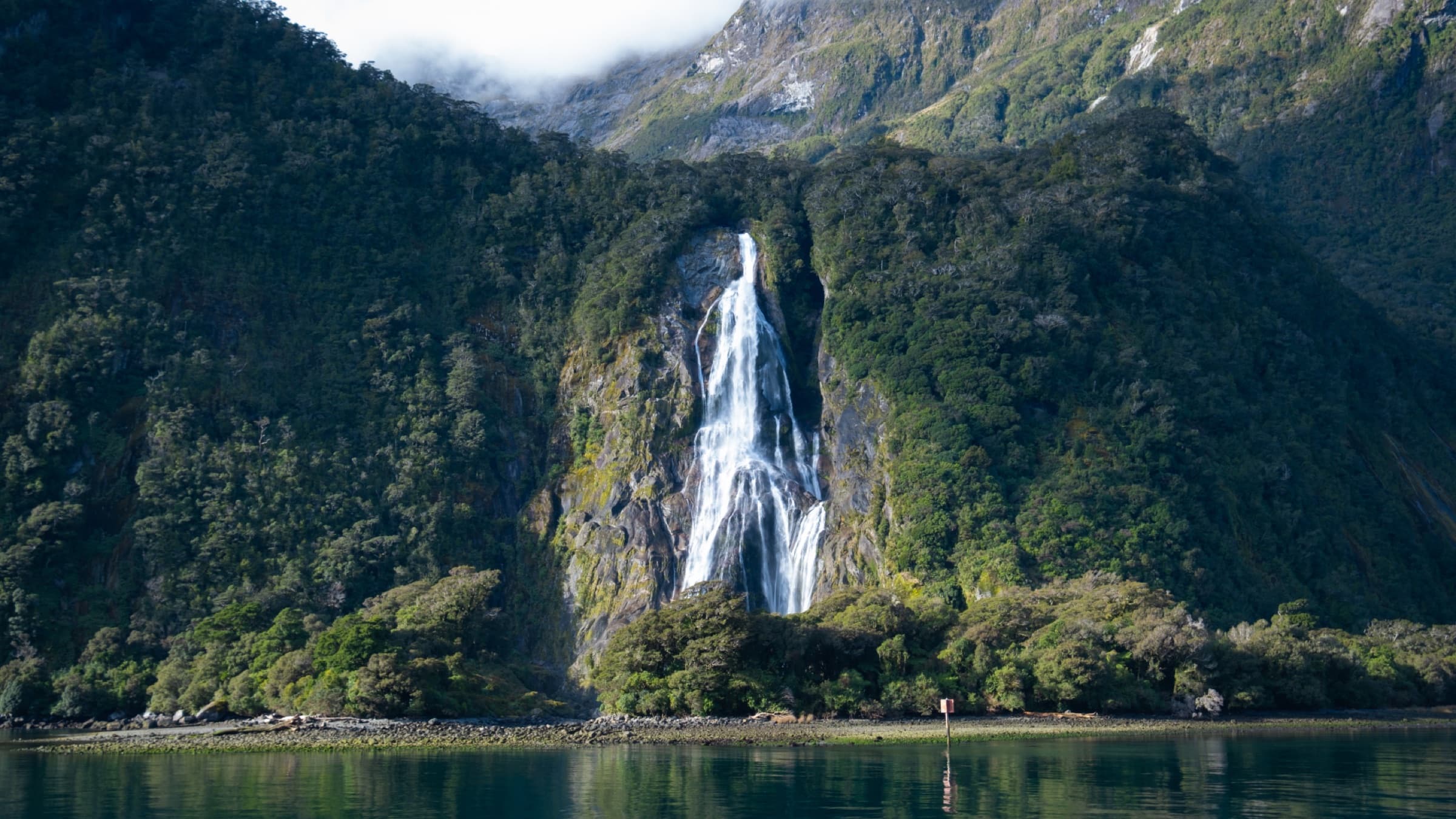 Misty fjord with a waterfall dropping through dark green cliffs into still water
